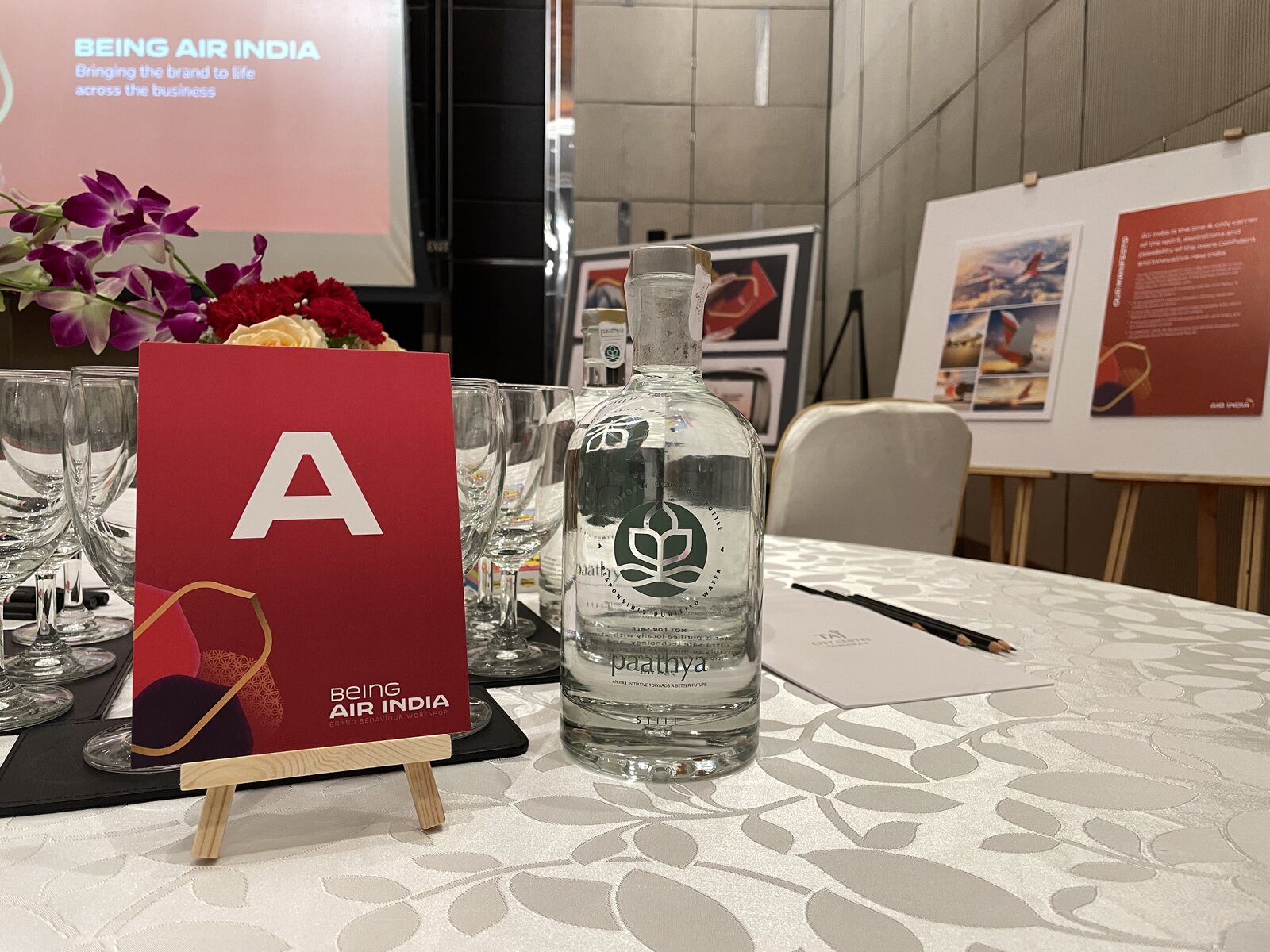 A place setting at the Being Air India brand behaviour workshop in Delhi, the red workshop card beside a reusable water bottle, with Air India brand boards on easels behind