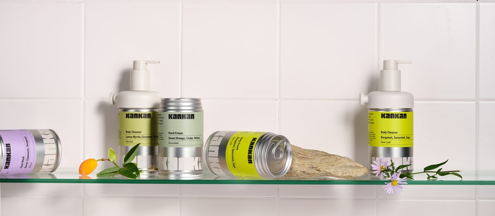 The Kankan body-care range on a glass shelf against white tiles, refillable bottles and cans styled with botanicals