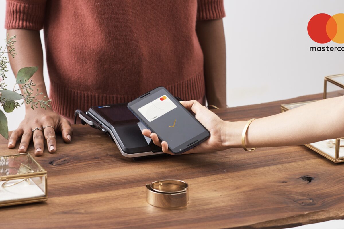 A contactless payment made with a phone at a card terminal, the Mastercard logo on a wooden counter