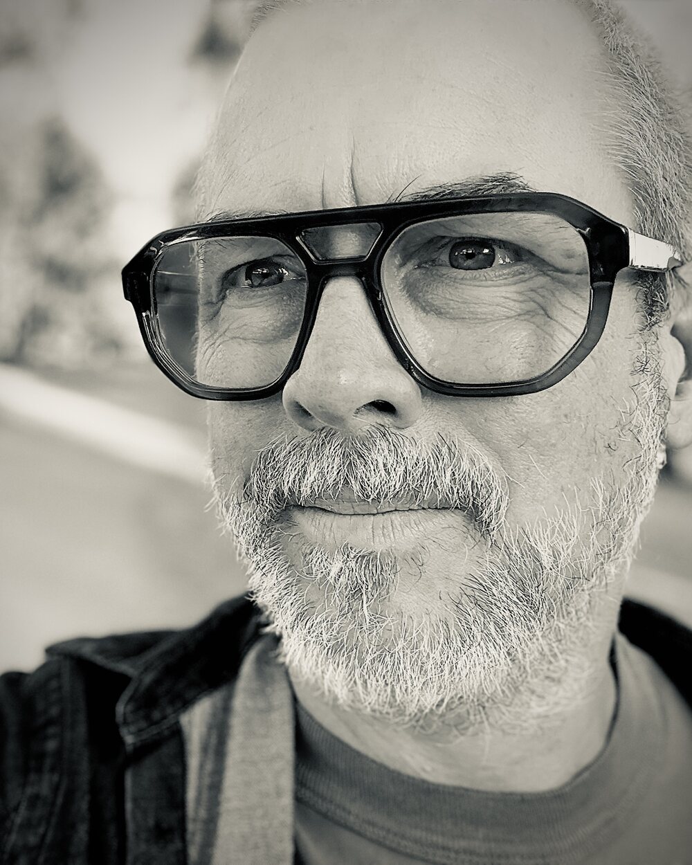 A black-and-white portrait of Stephen Barber, wearing glasses, outdoors